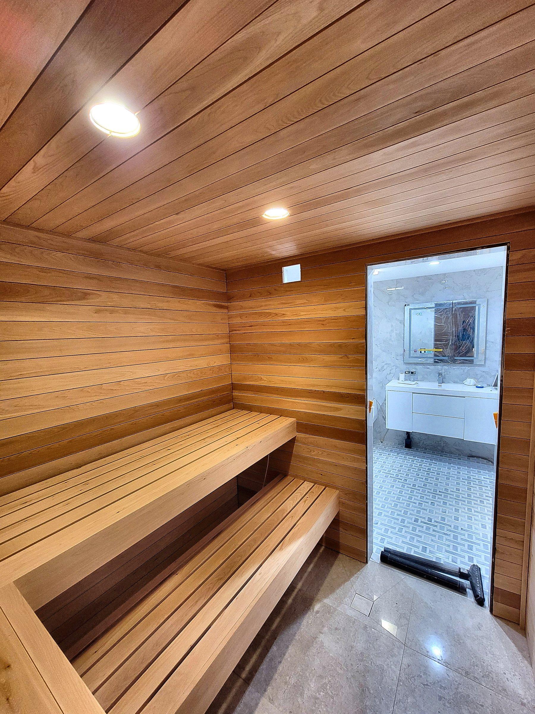 A cedar sauna in a corner, with tiered benches and a glass door.
