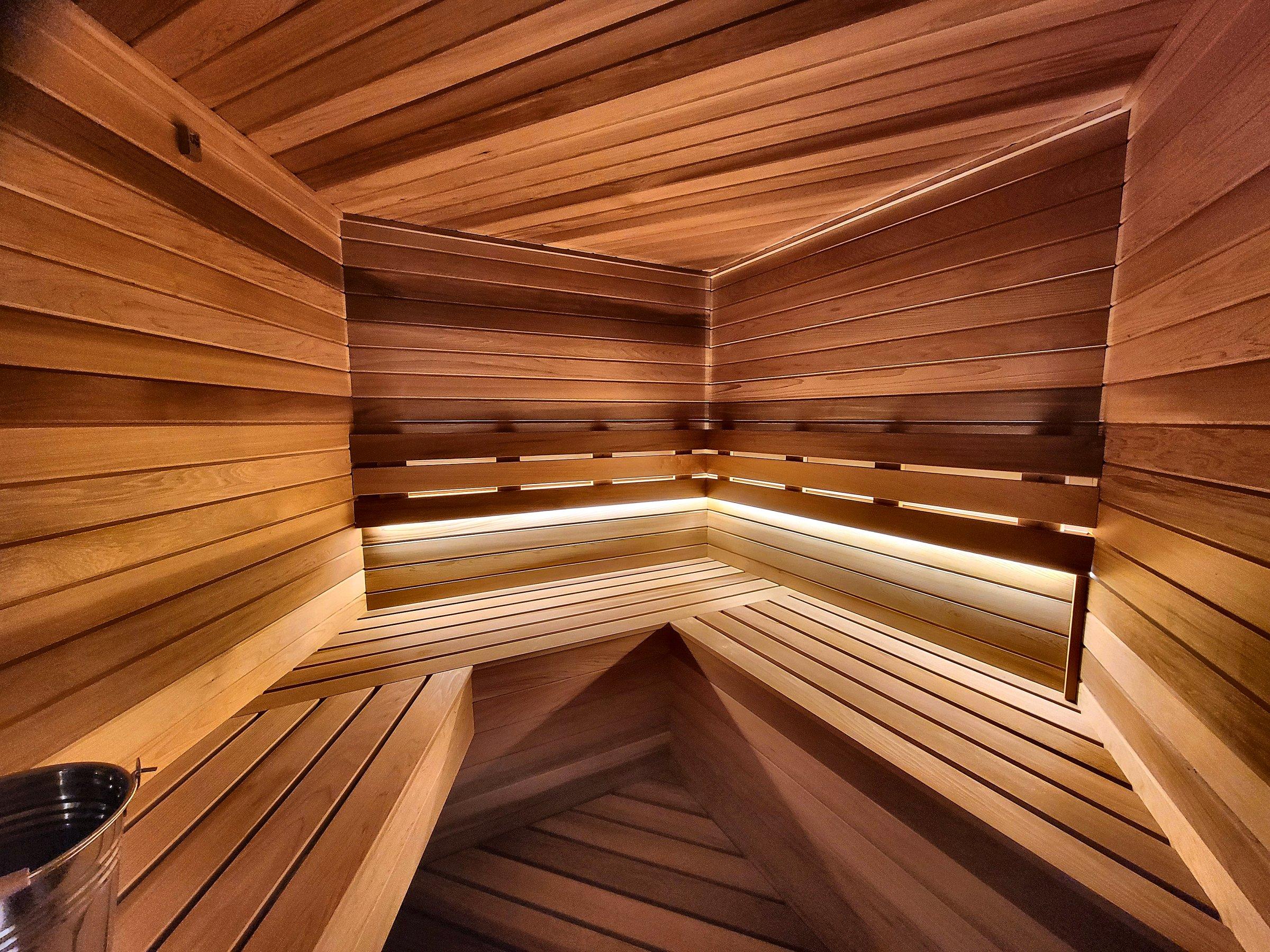 A cedar sauna with tiered benches and a light underneath the upper bench.