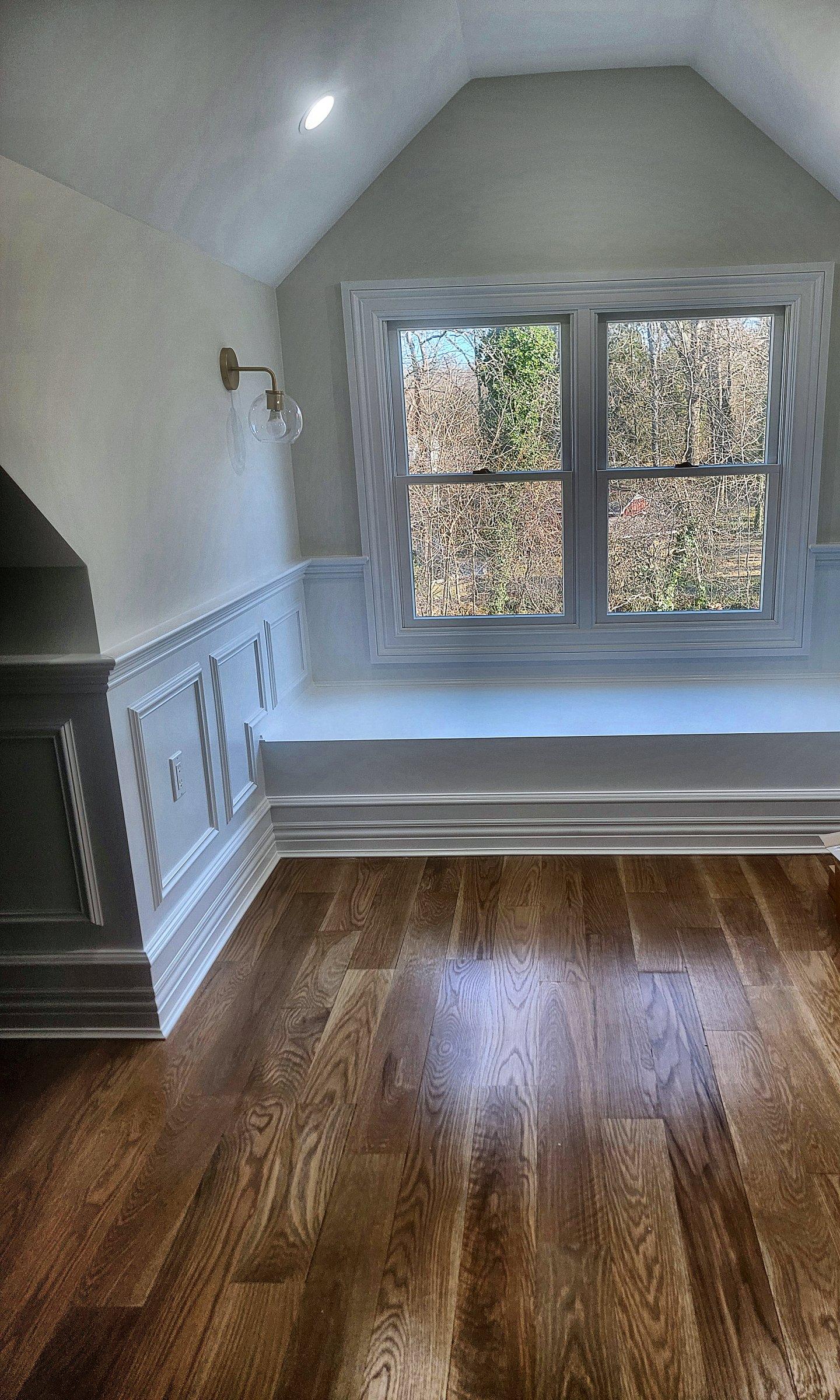 An attic window seat with a drawer below, under a sloped ceiling, with wainscot along the wall.