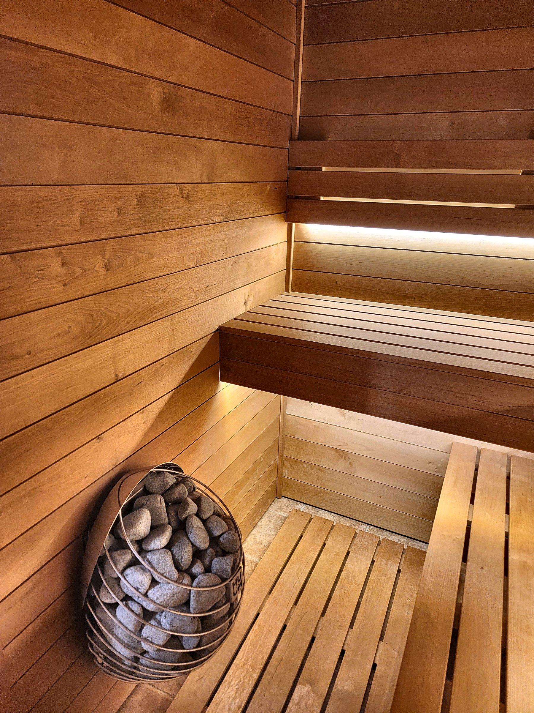 A cedar sauna with tiered benches, a light under the upper bench, and a heater filled with stones.