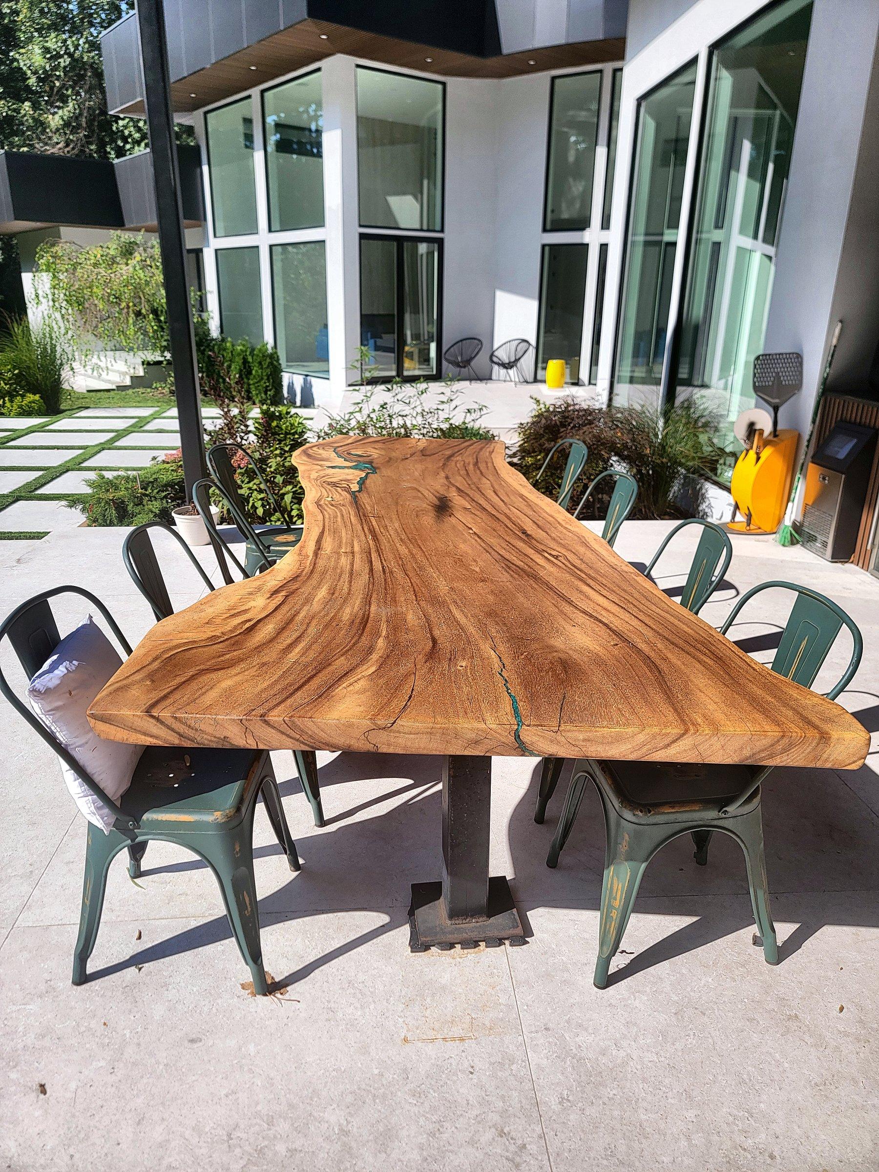 A live-edge slab table with a resin inlay, on hairpin legs, photographed on a patio.